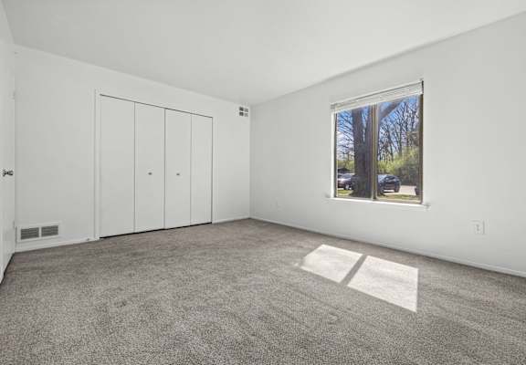 A room with a carpeted floor, a window, and a white door.