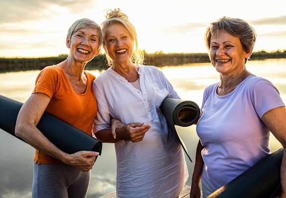 Three women are standing together holding yoga mats.