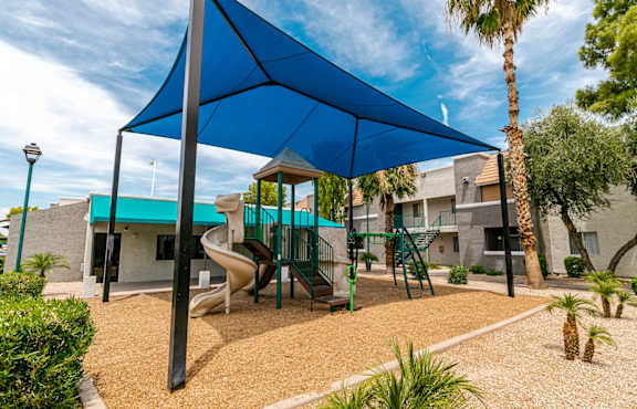 A playground with a blue shade structure and a slide.