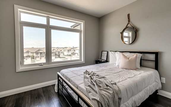 A bedroom with a large bed and a view of houses through the window.