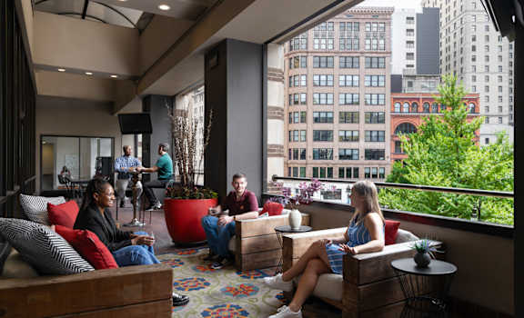 people sit on couches and chairs in a lobby with a large window