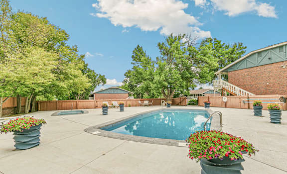 A pool surrounded by trees and concrete planters with flowers.