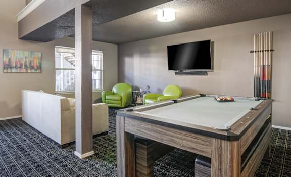 A billiard table is in the middle of a room with a TV mounted on the wall.