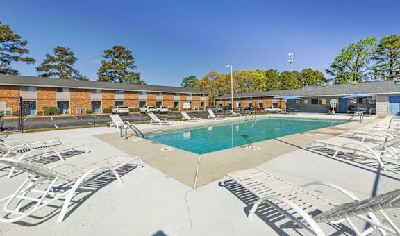 A pool surrounded by sun loungers and a building in the background.