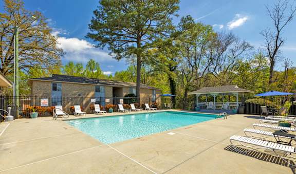 A swimming pool surrounded by trees and chairs.