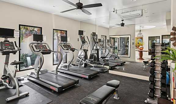 A spacious gym with treadmills, elliptical machines, and a ceiling fan.