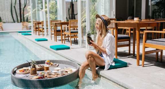 a woman sitting on the edge of a pool holding a pineapple