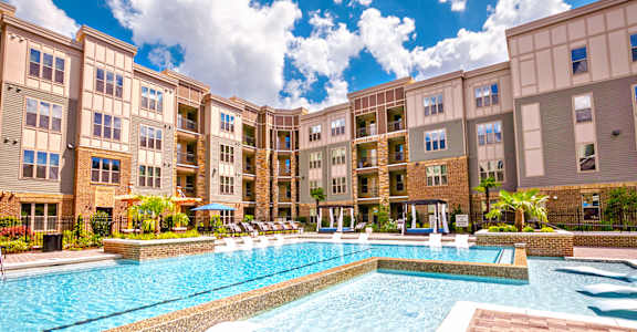 a swimming pool with lounge chairs and umbrellas in front of an apartment building