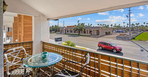 a balcony with a glass table and chairs and a red car parked on the street