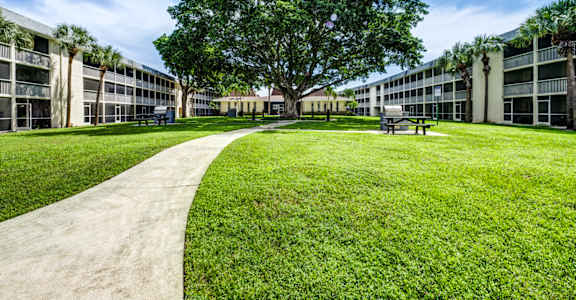 landscaped courtyard with green space and walking paths at Coronado Springs Apartments, a pet-friendly 1- and 2-bedroom community in Palm Springs, Florida.