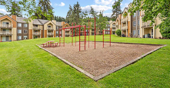 A playground with a red swing set in the middle of a grassy area at MonteVista Apartments, Oregon