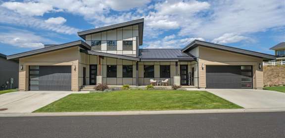 A modern house with a large front yard and two garages.