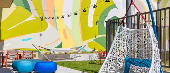 A white hanging chair with blue cushions is in the foreground of a colorful mural.