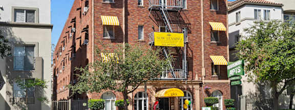A red brick building with a yellow awning and a sign that says "Now Leasing".