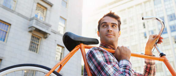 Lifestyle image of man in a button down shirt carrying an orange bike