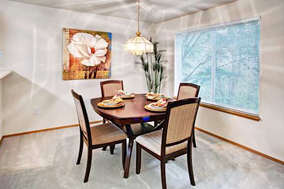 A dining room with a table set for two and a large painting on the wall.