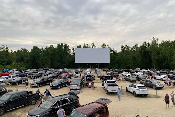 A large outdoor movie theater with cars parked in the parking lot and people walking around.