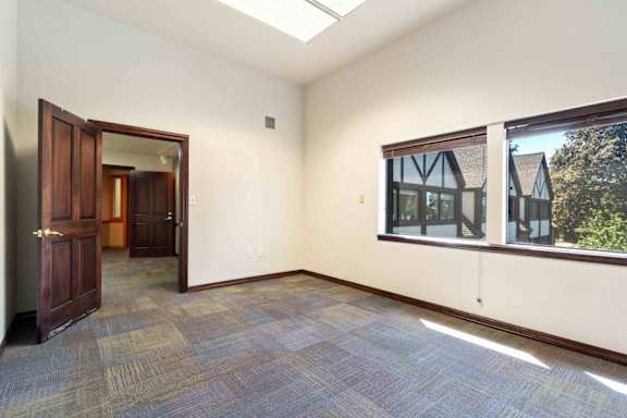 A room with a carpeted floor and a window showing a house.