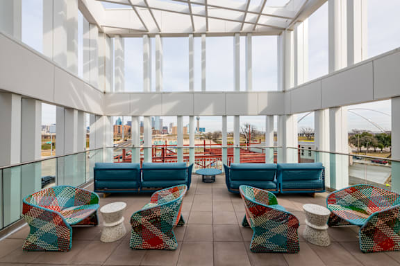A white building with a glass ceiling and colorful chairs and tables on the balcony.
