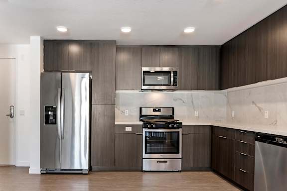 A modern kitchen with a stainless steel refrigerator, microwave, oven, and dishwasher at Fusion Hollywood.