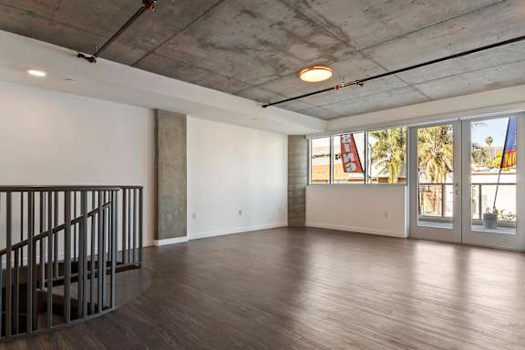 A large empty room with wooden floors and a staircase leading downward on the left side.
