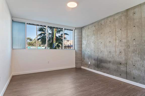 A bedroom with a concrete wall and a window at Fusion Hollywood.
