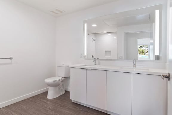 A white bathroom with a toilet, sink, and mirror at Fusion Hollywood.