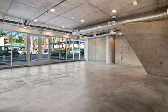 A large, empty room with a concrete floor and walls, and a glass door leading to a street in a live/work apartment at Fusion Hollywood.