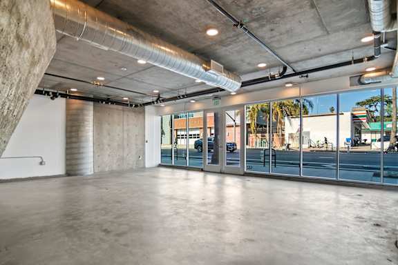 A large, empty room with a concrete floor and a glass wall overlooking a street in a live/work apartment at Fusion Hollywood.