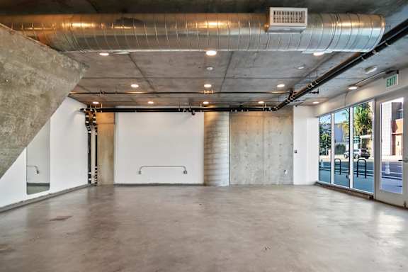 A large, empty room with a concrete floor and walls, and a metal pipe running along the ceiling in a live/work apartment at Fusion Hollywood.