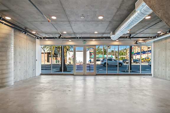 A large empty room with a concrete floor and ceiling, and a view of the outside through glass doors in a live/work apartment at Fusion Hollywood.