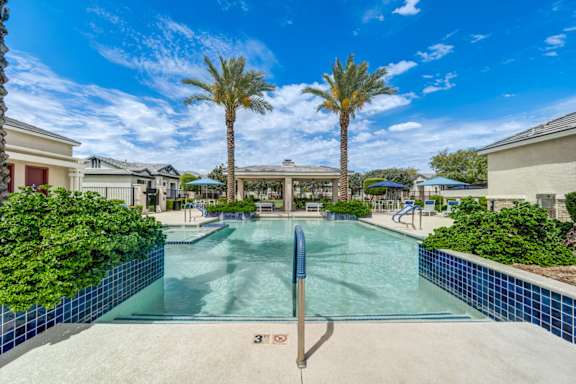 A swimming pool surrounded by palm trees and residential buildings.
