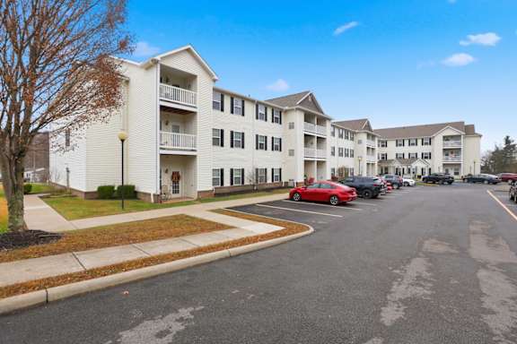 A red car is parked in the parking lot of a white apartment building.