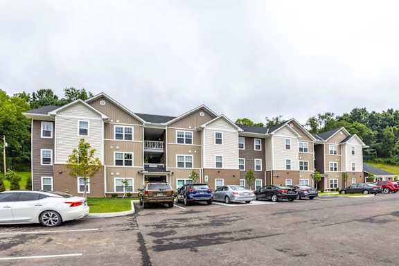 A parking lot in front of a two-story apartment building with cars parked in the lot.