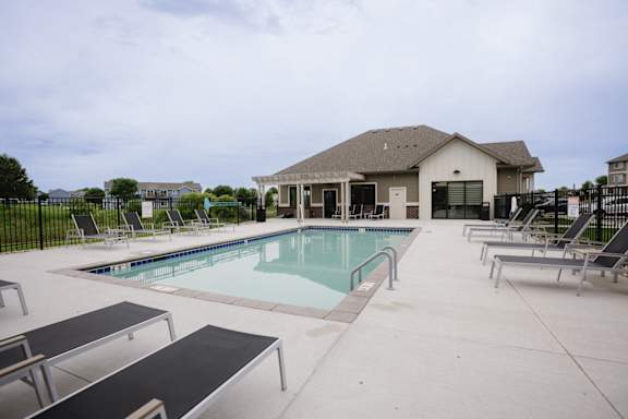 A pool with lounge chairs and a house in the background.