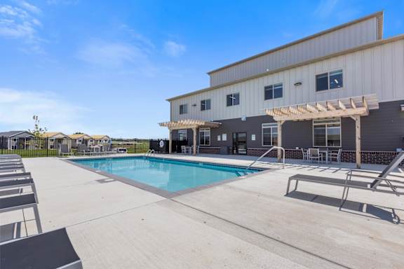 A pool area with sun loungers and a building in the background.