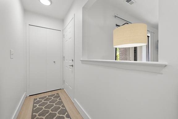 A hallway with a rug on the floor and a lamp on the wall.