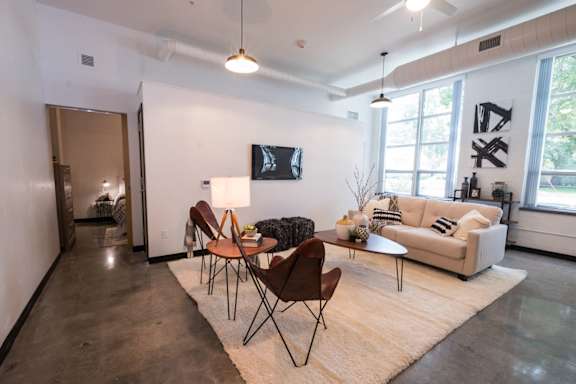 A living room with a white couch, a wooden table, and a TV mounted on the wall.