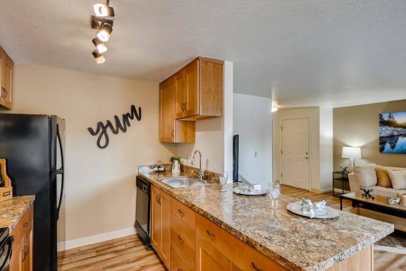 Happy Valley, OR, Apartments - Sunnyside Village - Kitchen with Wood-Style Flooring, Granite Countertops, Wood-Style Cabinetry, and Black Appliances.