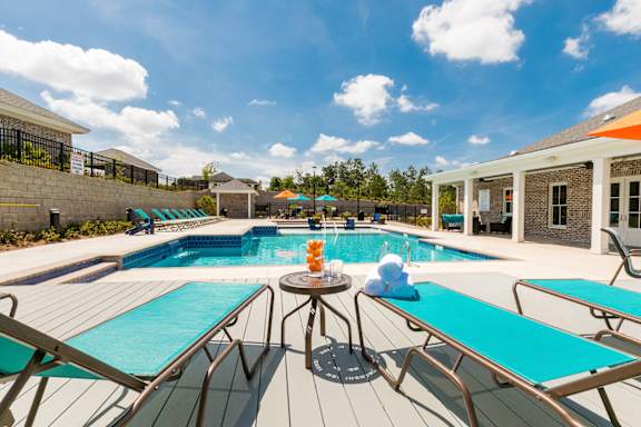 A poolside table with drinks and a sun lounger. at McHenry Square Apartments, Augusta, GA, 30909