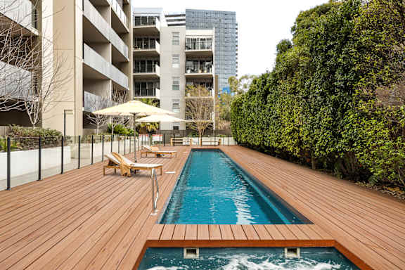 a swimming pool on a wooden deck next to an apartment building