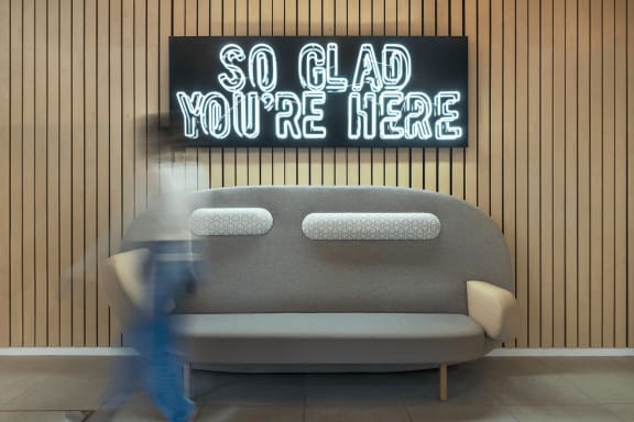 a neon sign that reads so glad you are here on a wall behind a couch