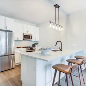 a kitchen with a large island with stools and a stainless steel refrigerator