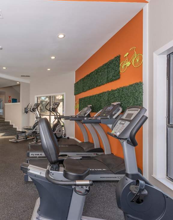 Fusion 35 Apartments gym with treadmills, bikes, and grass on an orange wall with a yellow bike.