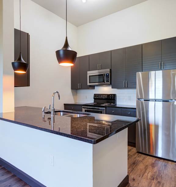 A modern kitchen with a stainless steel refrigerator and a black countertop.