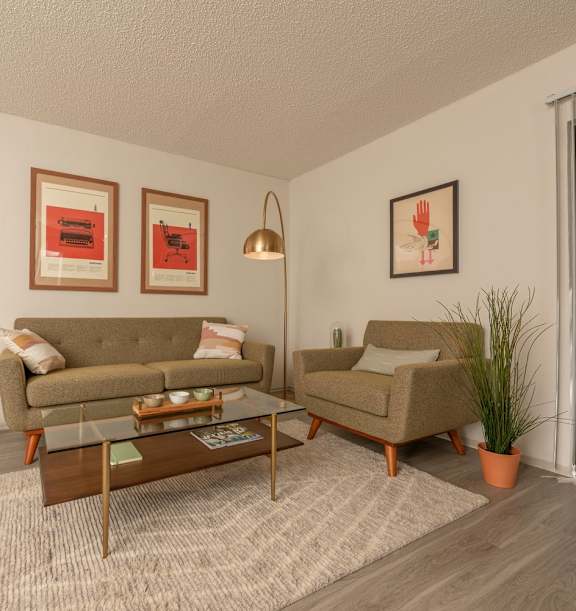 Fusion 35 Apartments staged living room with beige couches, two tables, and pictures on the walls.