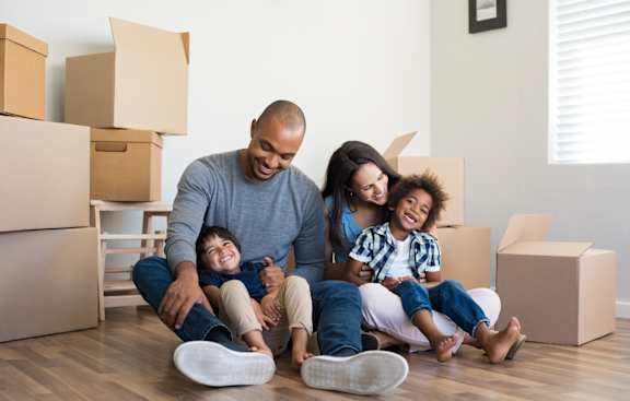 A family of four sitting on the floor surrounded by moving boxes.