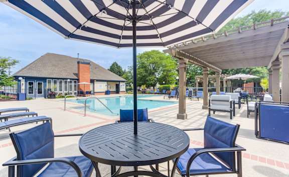 A black and white striped umbrella shades a table and chairs by a pool.