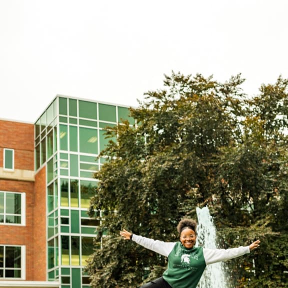 a woman jumping on a ledge in front of a fountain