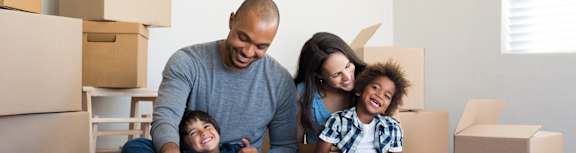 A family of four sitting on the floor surrounded by moving boxes.